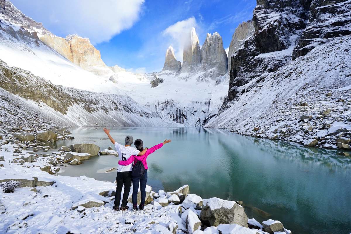 Ένα ζευγάρι ταξιδιωτών στέκεται κοιτάζοντας το Torres del Paine, μετά από μακρά πεζοπορία σε χιονισμένο μονοπάτι, στο εθνικό πάρκο Torres del Paine, Παταγονία, Χιλή.